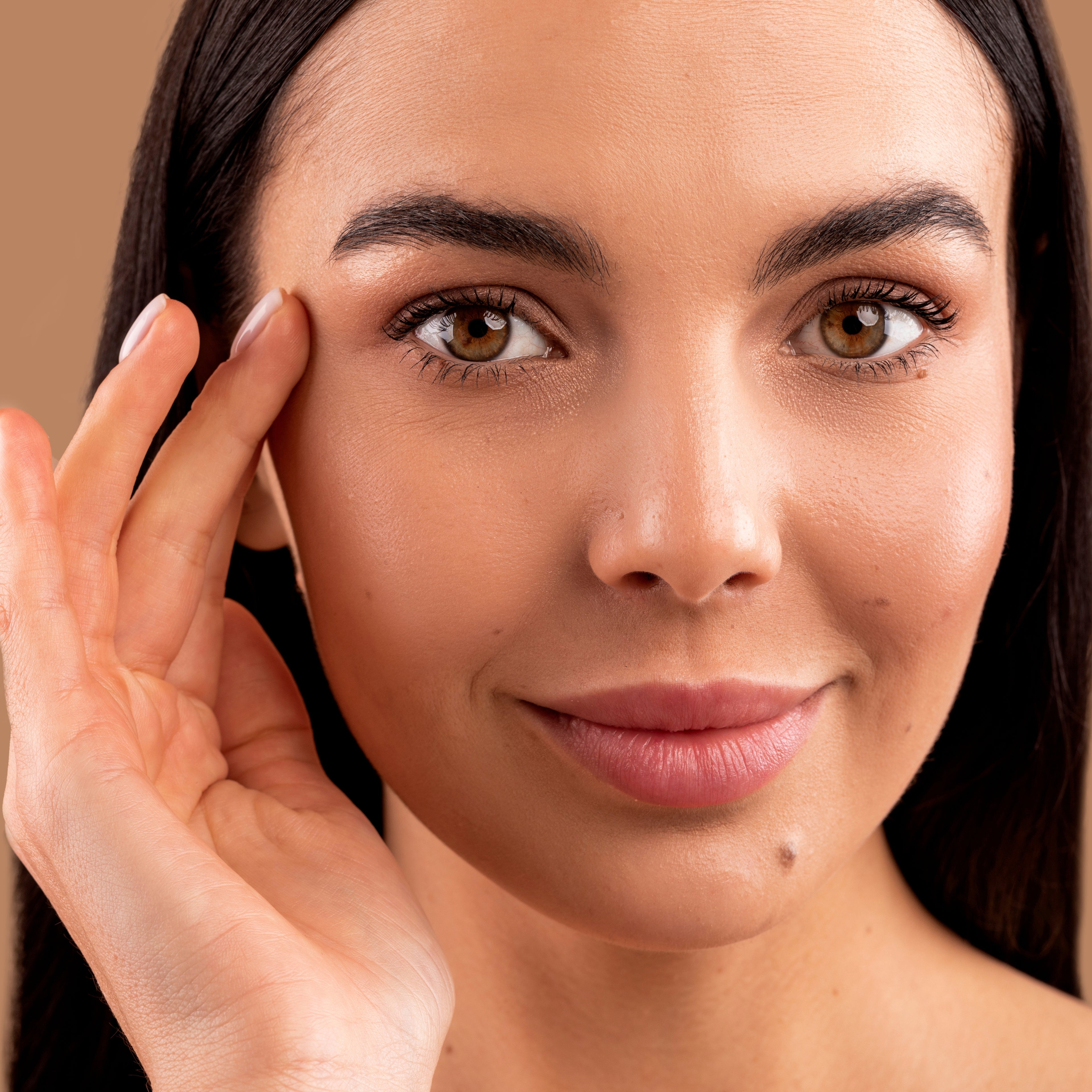 Woman with a hand next to her eye on a brown background.