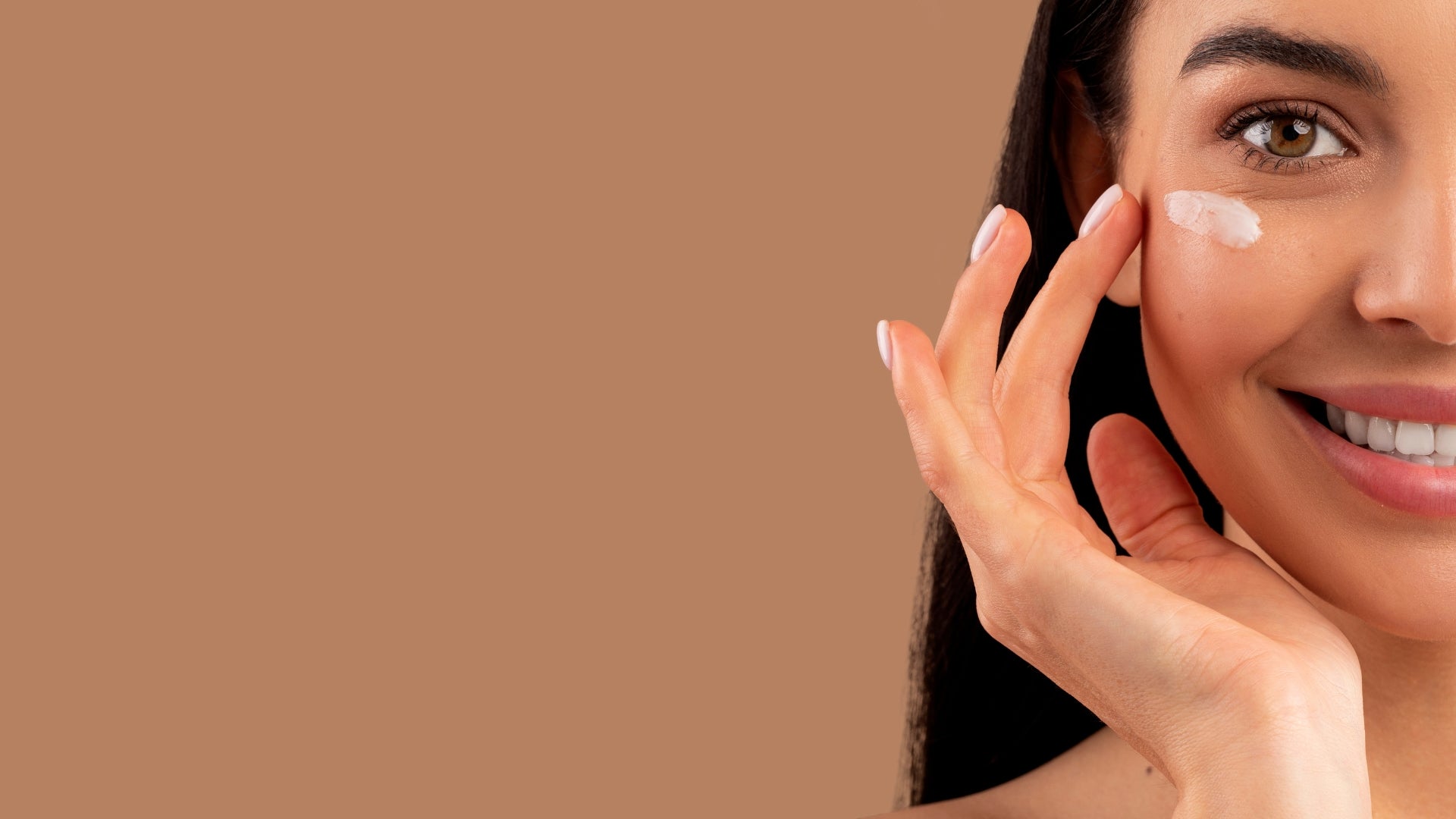 Woman applying cream to her face on a brown background.