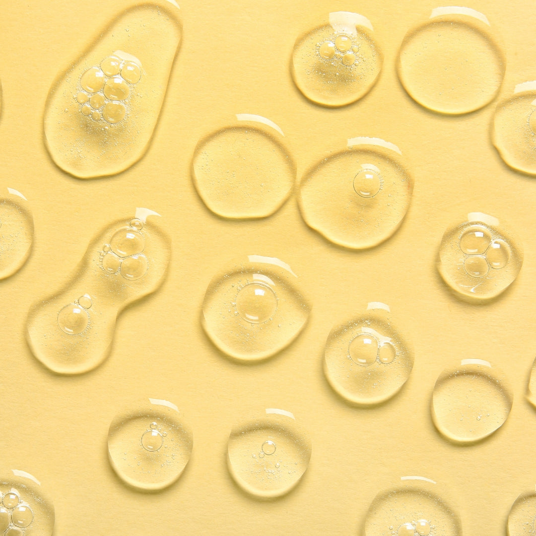 Closeup of clear liquid drops on a yellow background.