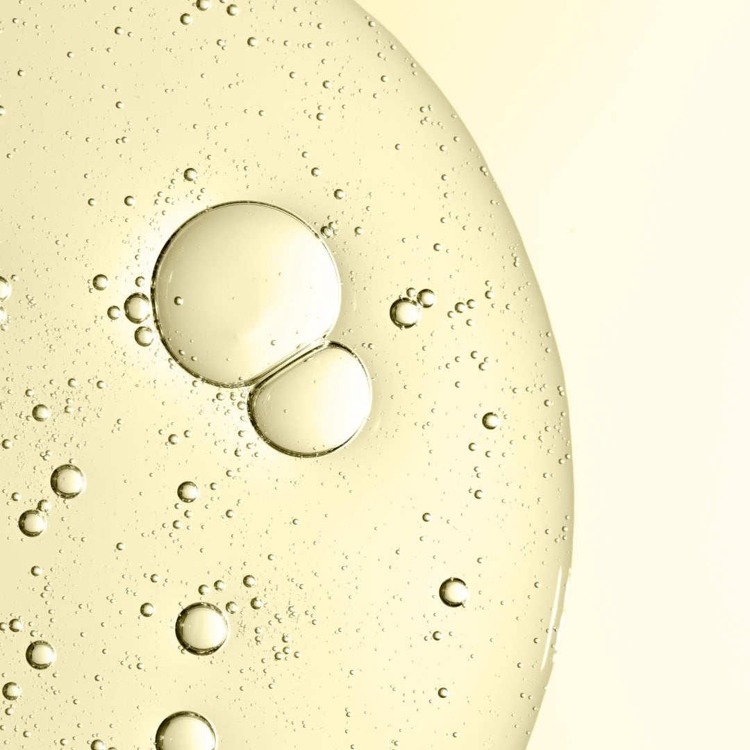 Closeup of yellow liquid bubbles on a light yellow background.